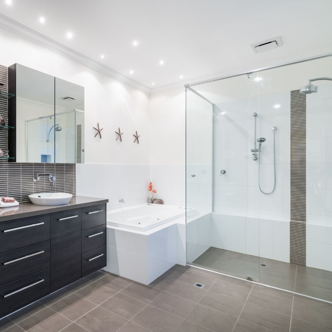 Salle de bain avec des plafonniers au-dessus de la baignoire, du meuble-lavabo et de la cabine de douche.