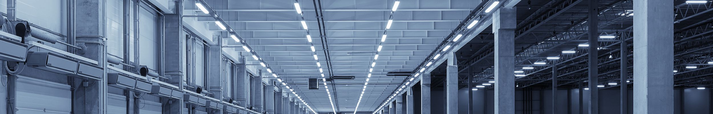 Interior empty industrial warehouse with large delivery doors on left and LED battens across ceiling