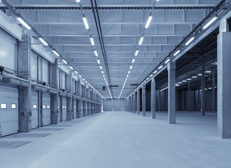 Interior empty industrial warehouse with large delivery doors on left and LED battens across ceiling