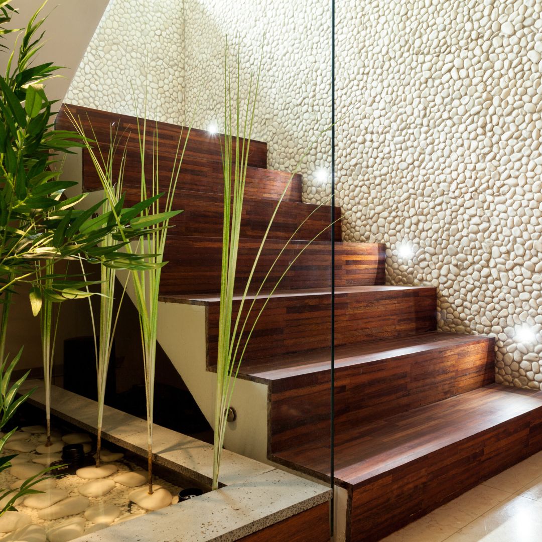 Exterior stairwell with plants and wooden steps. Stair lights embedded in white pebble wall provide illumination